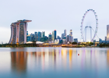 Singapore City Skyline with Marina Bay Sands hotel (left) and the Singapore Flyer ferris wheel, showing reflection in the still water at twilight