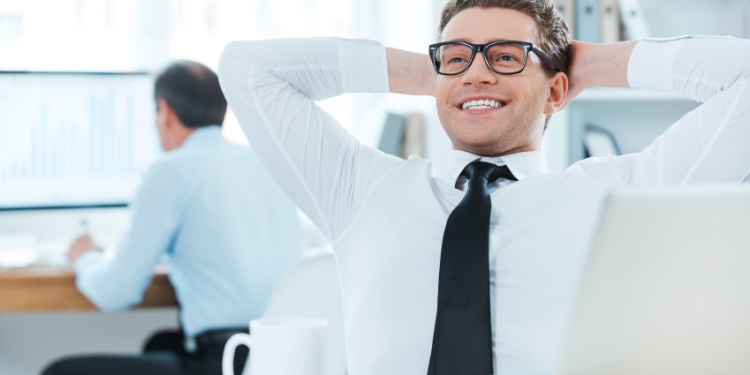 Satisfied with the work done. Cheerful businessman in formalwear holding head in hands while sitting at his desk in the office