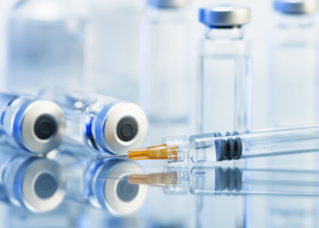 Syringe. Disposable plastic medical syringe surrounded by sealed medication vials.