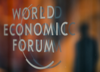 A person is reflected in a window with the logo of the World Economy Forum on the last day of the forum's Annual Meeting in Davos, Switzerland, Friday, Jan. 19, 2024. (AP Photo/Markus Schreiber)