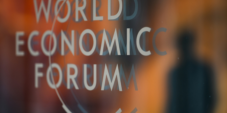 A person is reflected in a window with the logo of the World Economy Forum on the last day of the forum's Annual Meeting in Davos, Switzerland, Friday, Jan. 19, 2024. (AP Photo/Markus Schreiber)